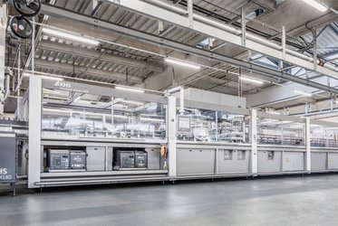 Das Bild zeigt eine große, moderne KHS-Maschine in einer industriellen Produktionshalle, die für die Verarbeitung und Verpackung von Produkten eingesetzt wird, umgeben von hellen Deckenleuchten und Metallstrukturen.